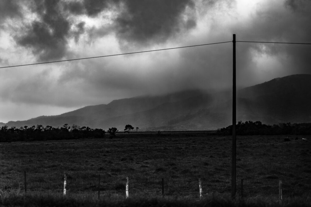 Paisagem em preto e branco de montanhas sob a neblina e um campo largo.